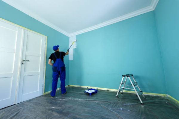 Man in a working overall is painting the wall in white color Man in a working overall is painting the wall in white color